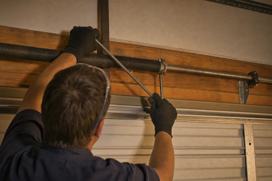 Technician fitting winding bars to a torsion spring above a closed garage door in Sapulpa